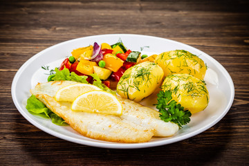 Fish dish - fried cod fillet with potatoes and vegetables on wooden table
