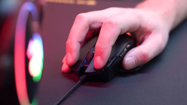 A gamer is playing in a computer club. In the frame, the hand of a gamer and a gaming mouse. Red and violet colors. ESports competitions.


