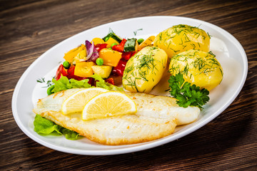 Fish dish - fried cod fillet with potatoes and vegetables on wooden table
