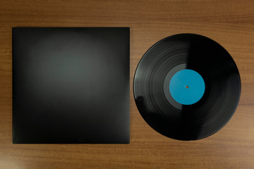 Empty Black Vinyl disk case and vinyl with blue tag in a wood background for mockup purposes