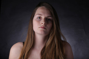 Fototapeta premium Studio portrait of young girl with light hair and freckles, with dark background.