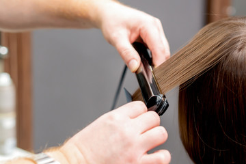 Hairdresser straightens hair of woman.