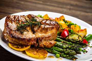 Barbecue beef steak fried potatoes and vegetables on wooden table