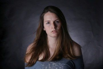 Fototapeta premium Studio portrait of young girl with light hair and freckles, with dark background.