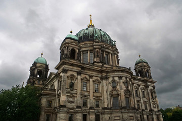 Fototapeta na wymiar View of the upper part of the cupola of the Berlin Cathedral with the turquoise copper roof and golden cross on top in front of an impressive sky with white grey clouds; Berlin, Germany, Europe 