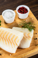 Fresh raw cod with seasonings and vegetables served on cutting board on wooden table

