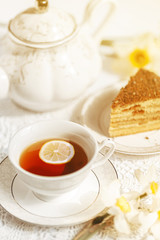 Closeup slice of lemon in a cup of tea on a background of flowers and a teapot