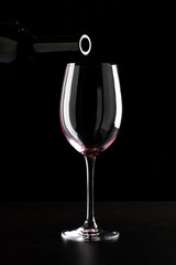 Red wine being poured into a glass and splashing over the side. Low key black background.