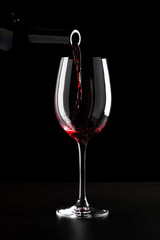 Red wine being poured into a glass and splashing over the side. Low key black background.
