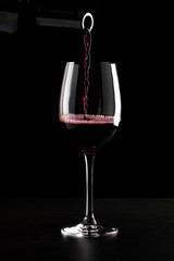 Red wine being poured into a glass and splashing over the side. Low key black background.