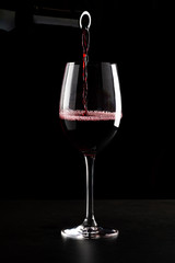 Naklejka na ściany i meble Red wine being poured into a glass and splashing over the side. Low key black background.