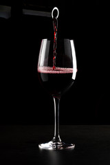 Red wine being poured into a glass and splashing over the side. Low key black background.