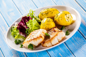 Fish dish - fried cod fillet with potatoes and vegetables on wooden table
