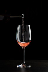 Rose wine pouring in a glass on black background