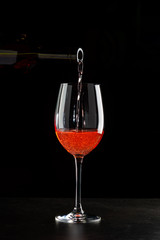 Rose wine pouring in a glass on black background