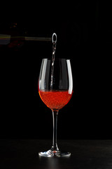 Rose wine pouring in a glass on black background