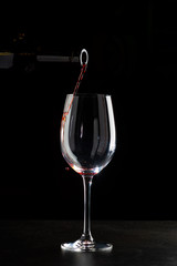 Red wine pouring into a glass with drops on black background