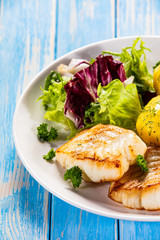 Fish dish - fried cod fillet with potatoes and vegetables on wooden table
