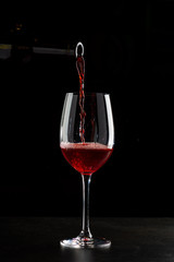 Red wine pouring into a glass with drops on black background