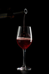 Red wine pouring into a glass with drops on black background