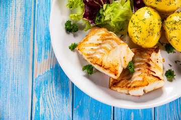 Fish dish - fried cod fillet with potatoes and vegetables on wooden table
