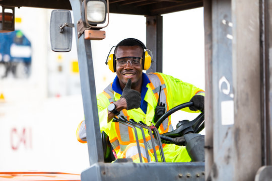 African American Man At Work. Professional Operation Engineering. Young Worker Forklift Driver Wearing Safety Goggles And Hard Hat Sitting In Vehicle In Warehouse