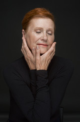 Red-haired elderly lady in a black sweater on a dark gray background