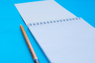 An opened caged notebook with pencil over turquoise background. Selective focus.