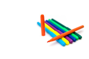 Colorful markers lying in a row on a white background. Opened orange marker lies on top of the...