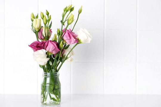 A glass vase with eustomia purple and white flowers on white background
