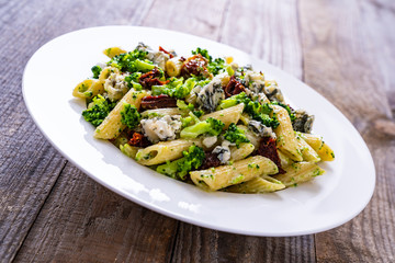 Penne with gorgonzola broccoli and sun-dried tomatoes on wooden table