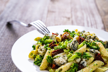 Penne with gorgonzola broccoli and sun-dried tomatoes on wooden table