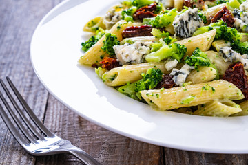 Penne with gorgonzola broccoli and sun-dried tomatoes on wooden table