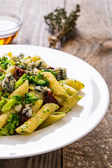 Penne with gorgonzola broccoli and sun-dried tomatoes on wooden table