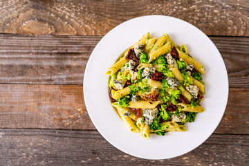 Penne with gorgonzola broccoli and sun-dried tomatoes on wooden table