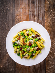 Penne with gorgonzola broccoli and sun-dried tomatoes on wooden table