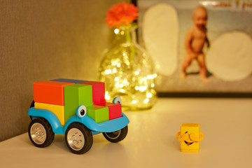 Wooden toy car on a blurred background of a child’s photo and an orange flower in a glass bottle with backlight