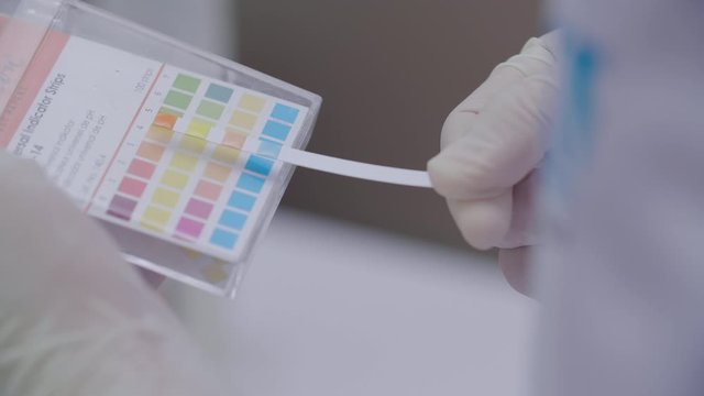 Analytical scientist doing a litmus paper test at a laboratory to test pH level using universal test paper and compares result to the chart.