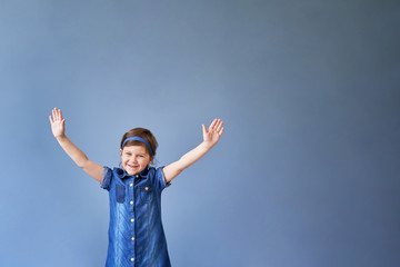 a little funny girl raised her hands up and is happy on a blue background