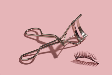 A metal lash curler with false lashes composition on pink background