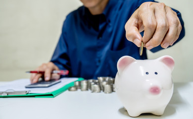 Saving money concept,Man hand putting coin drop into piggy bank and accounting calculate calculator...