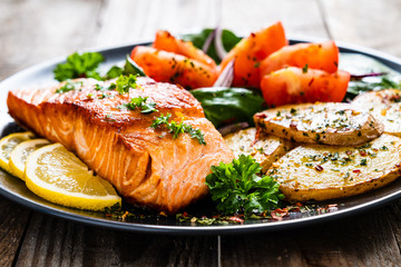 Fried salmon steak with potatoes and vegetables on wooden table