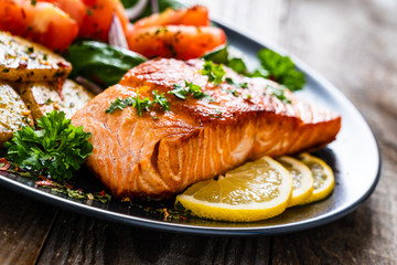 Fried salmon steak with potatoes and vegetables on wooden table