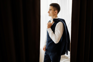 Grooms morning preparation. Preparation of groom before wedding at home. Stylish groom posing near window. Groom getting ready in the room for wed day. Copy space.