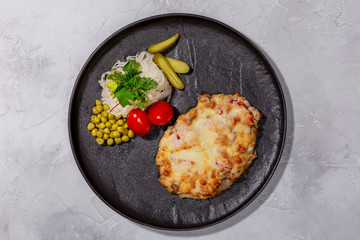 Baked pork with pineapple, mushrooms, tomato slices, cheese, side dish of pickles, green peas and salted cabbage. European cuisine. The work of a professional chef. Dish from a restaurant menu