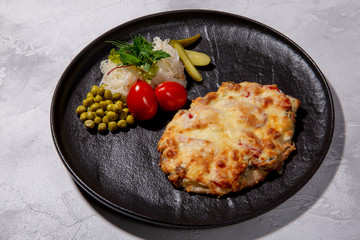 Baked pork with pineapple, mushrooms, tomato slices, cheese, side dish of pickles, green peas and salted cabbage. European cuisine. The work of a professional chef. Dish from a restaurant menu