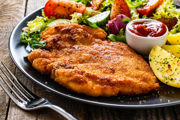 Pork chop with boiled potatoes and vegetable salad on wooden background
