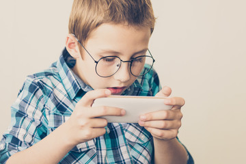 Handsome boy in glasses plays tablet. The concept of poor eyesight, harm of gadgets, autism