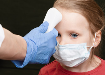 Doctor using infrared thermometer checking body temperature of little girl wearing surgical mask -...