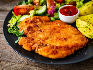 Pork chop with boiled potatoes and vegetable salad on wooden background
